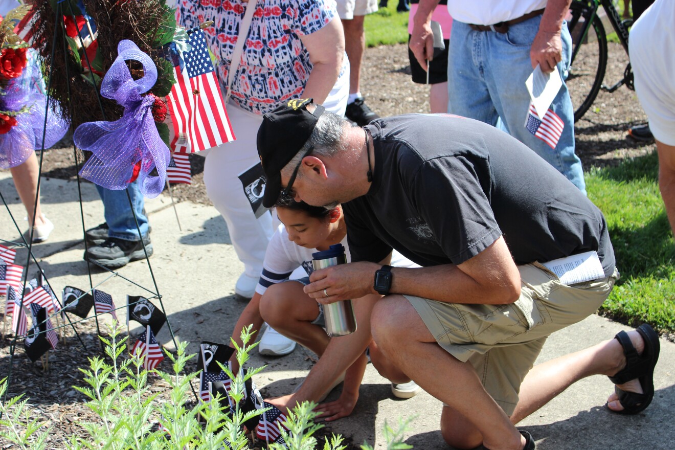Generations young and old place USA and POW/MIA flags at the base of the memorial.